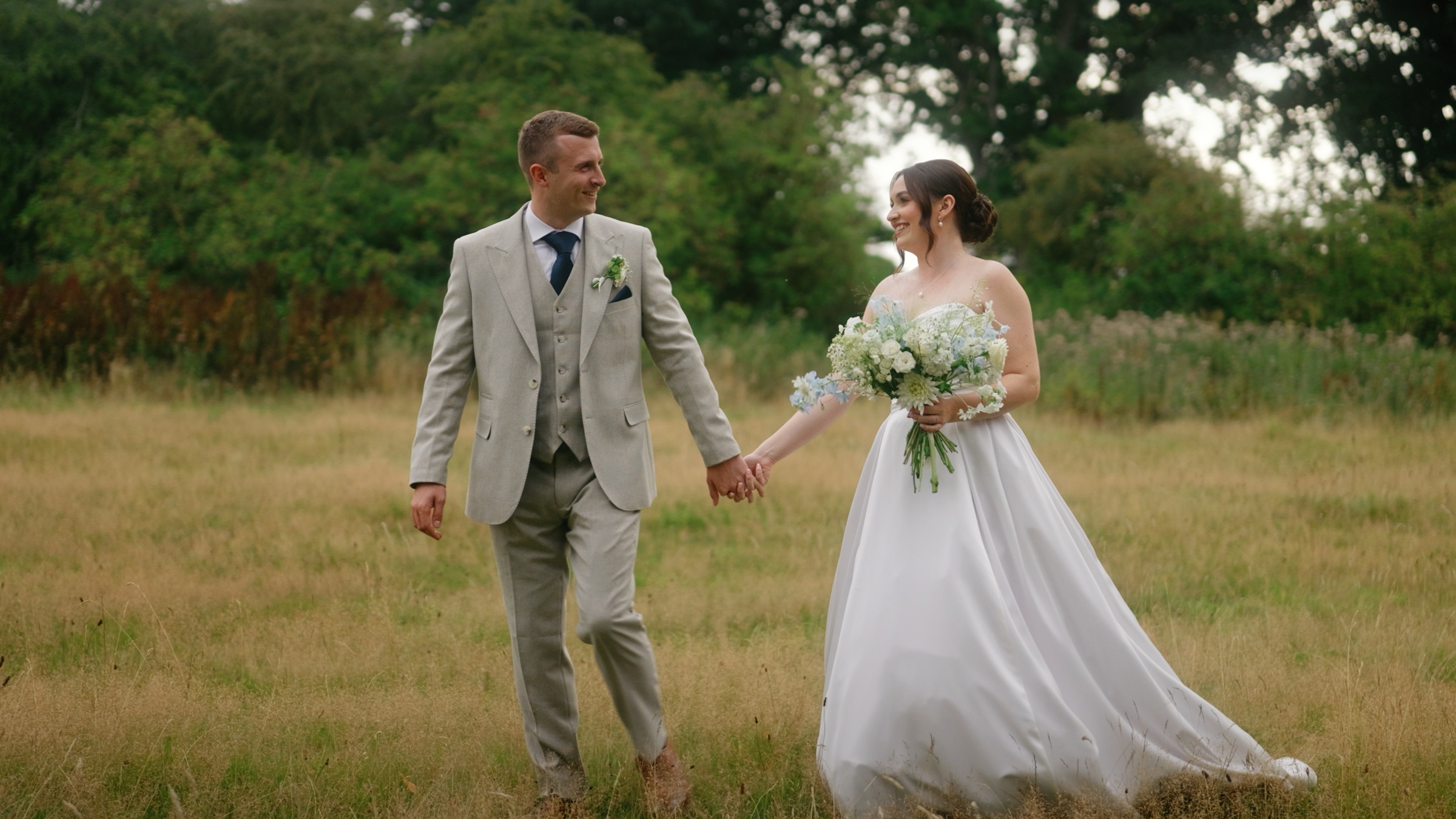 Emily and Josh walking hand in hand through the meadow at Aswarby Rectory